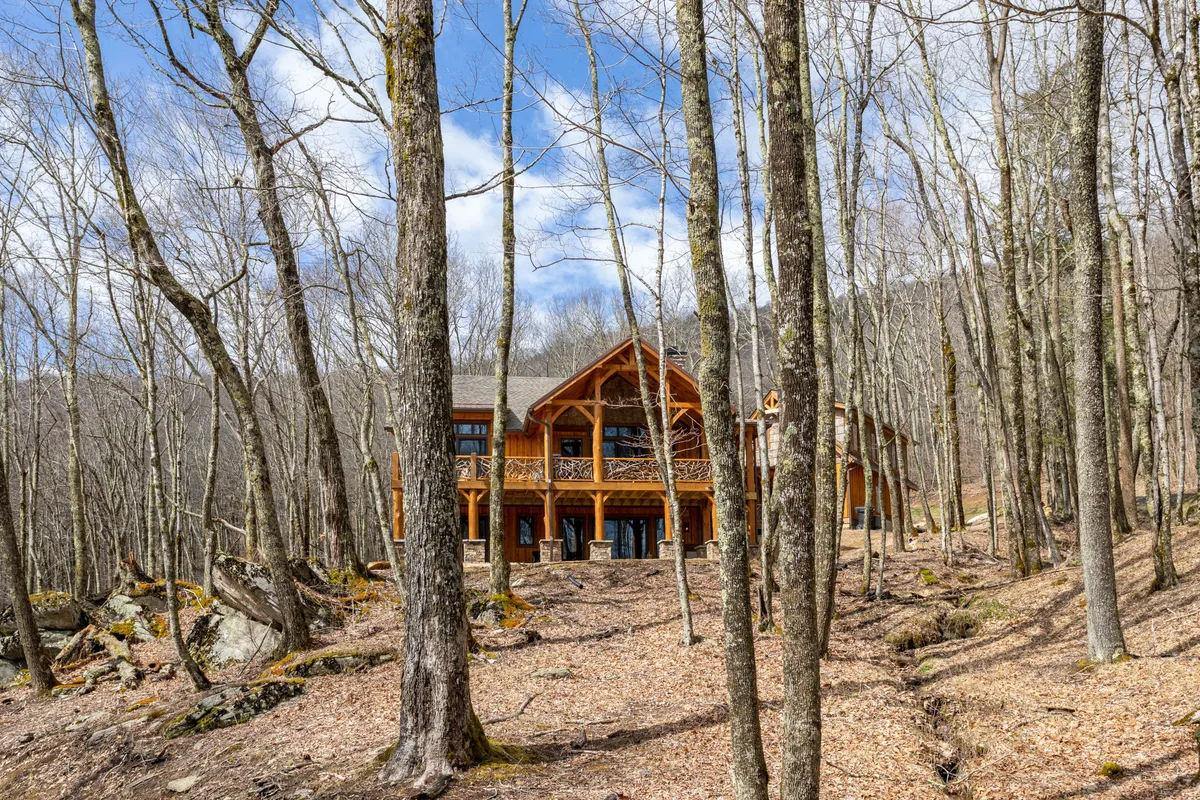 A welcoming wooden cabin sits nestled among tall trees and rocky terrain, evoking the sense of adventure and immersion in nature. The cabin's porch provides a clear launching point for hikes or wildlife observation, surrounded by the tranquil North Carolina mountain landscape.