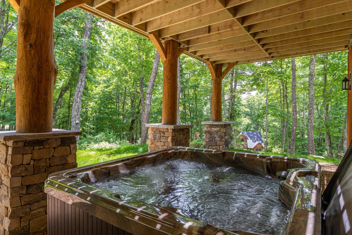 A private hot tub sits under rustic wooden beams and stone pillars, surrounded by lush greenery. This tranquil outdoor amenity offers a serene place to relax and rejuvenate after a day of adventure.