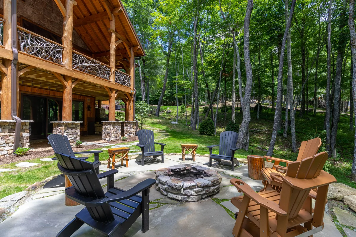 A welcoming fire pit area surrounded by Adirondack chairs, with the cabin's wooden structure and a backdrop of tall trees providing a cozy, nature-infused setting. The scene is perfect for evening gatherings, storytelling, and relaxing with friends or loved ones under the stars.