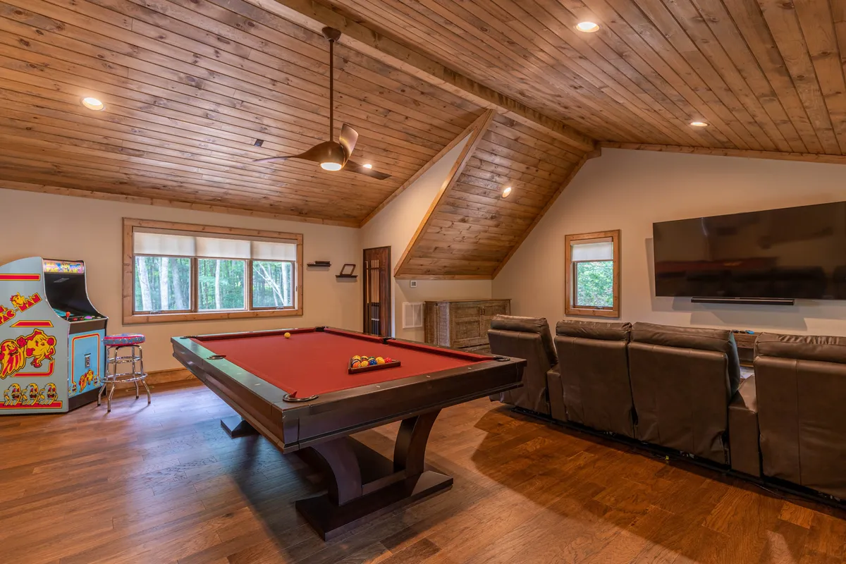 A flexible bonus room with a pool table, arcade game machine, large television, and comfortable seating. The space is bright and casual, suitable for both sleeping needs and entertainment.