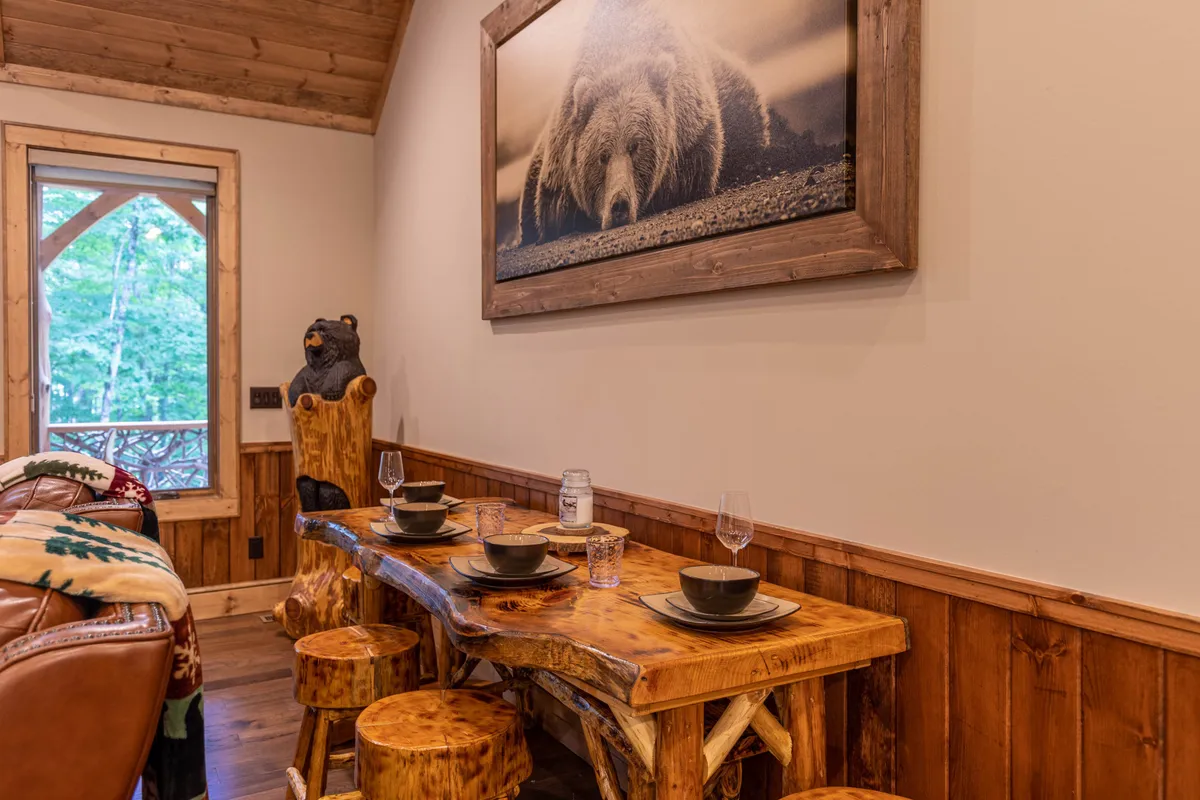 A rustic wooden dining table surrounded by matching chairs sits beneath warm lighting. A striking bear photograph on the wall adds a touch of local character. The setting radiates warmth and is ideal for family meals or celebrating special occasions.