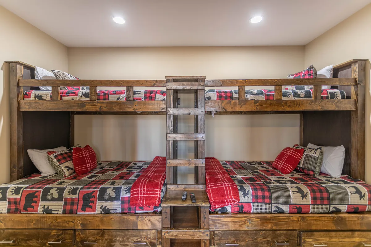 A playful bunk room featuring built-in bunk beds with plaid bedding, a sturdy wooden ladder, and space for both sleeping and play. The design is inviting and fun, ideal for kids or teens to build memories.