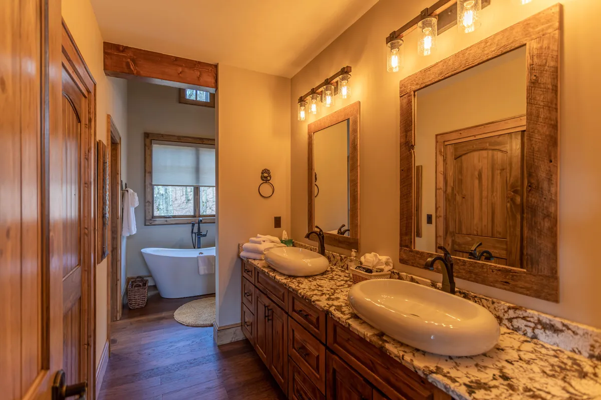 A serene bathroom with double sinks topped by round basins, large mirrors, a freestanding bathtub, and warm wooden accents. The layout is bright and spa-like, perfect for relaxation and self-care.